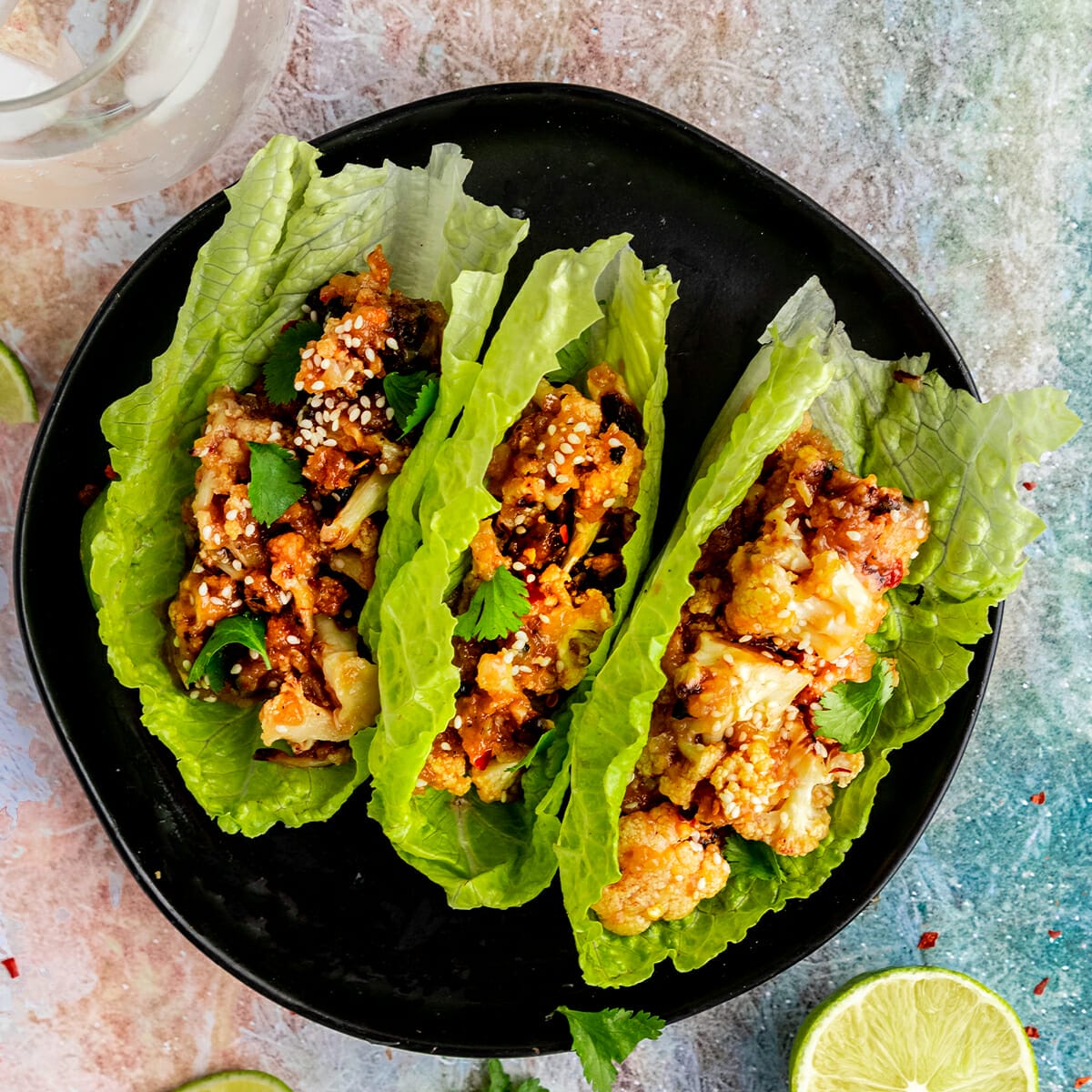 three lettuce wraps filled with sticky sesame cauliflower on a black plate