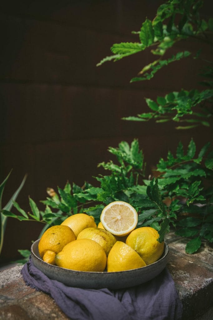 bowl of lemons on a brick table next to a tree