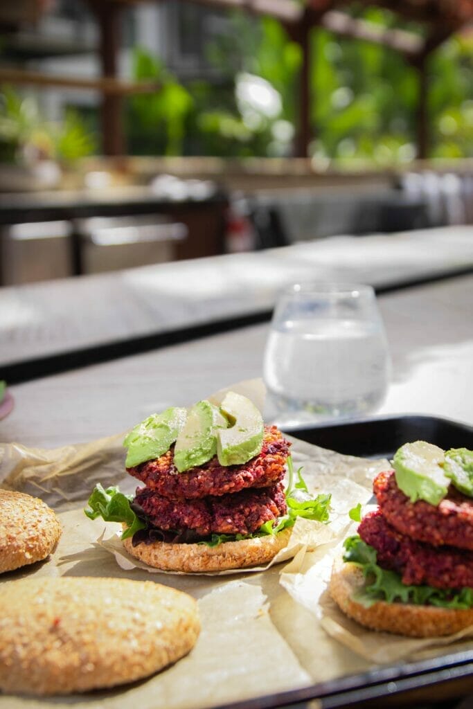 side view of a quinoa beet burger on a bun topped with three avocado slices
