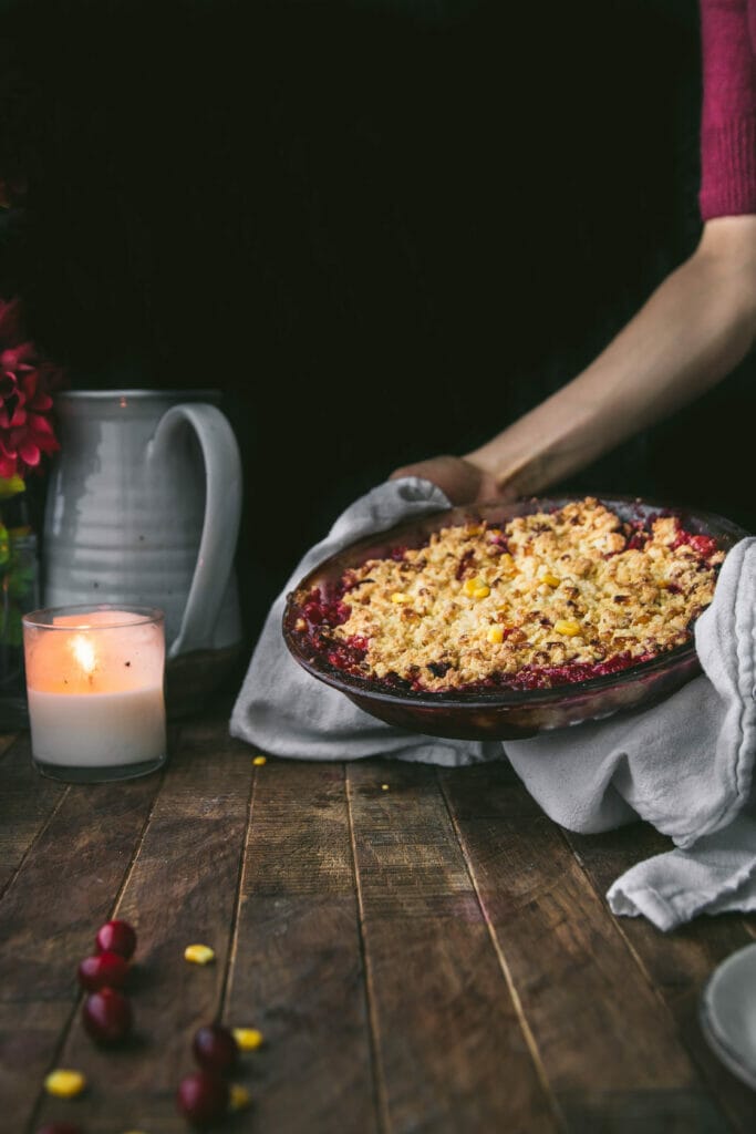 hands holding a plate of cranberry cornbread crisp placing it down on a wooden table