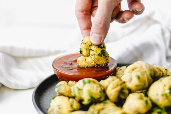 hand dipping garlic knot into red sauce