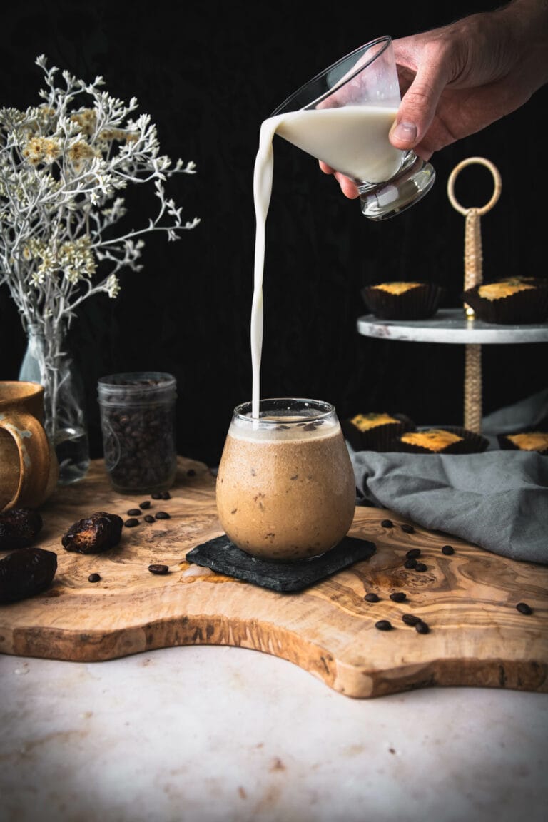 hand pouring milk into an iced coffee shake on a wooden table