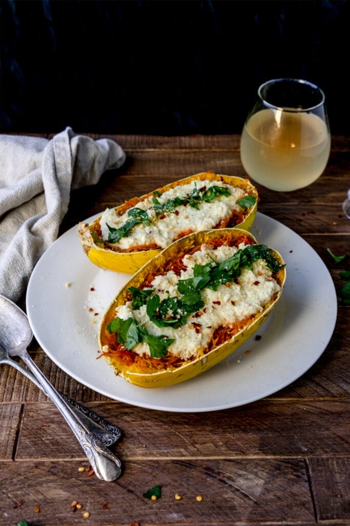 two spaghetti squash lasagnas with cashew cheese and topped with parsley on a white plate on a wooden table