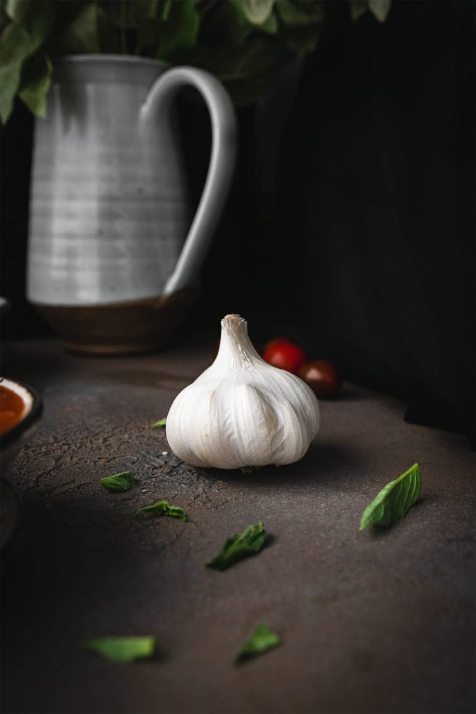 a whole head of garlic on a stone board next to some basil leave