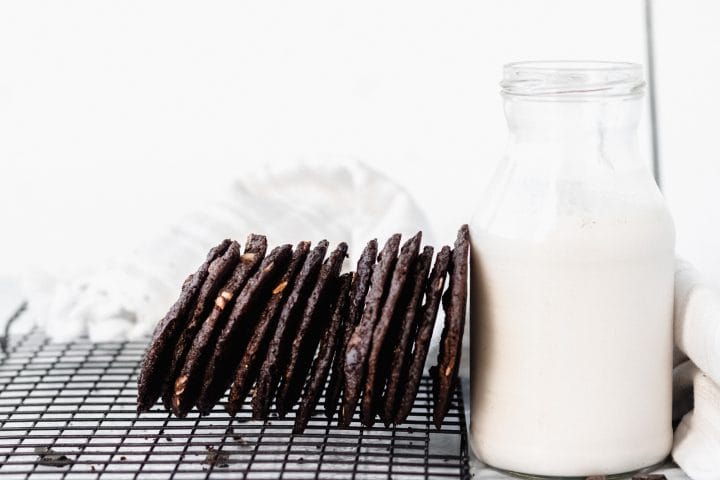 stack of tates cookies with chocolate next to a jug of milk