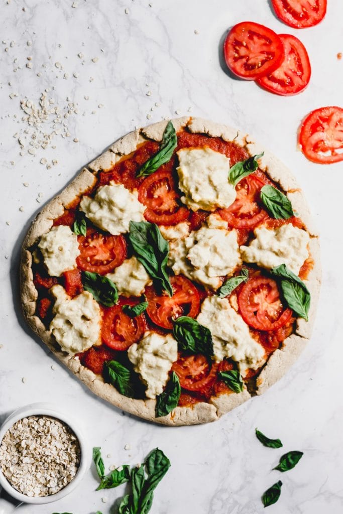 classic vegan pizza on white board with cheese and tomatoes