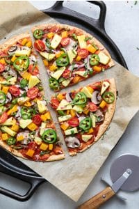 cast iron pan with parchment paper and sliced colorful veggie pizza
