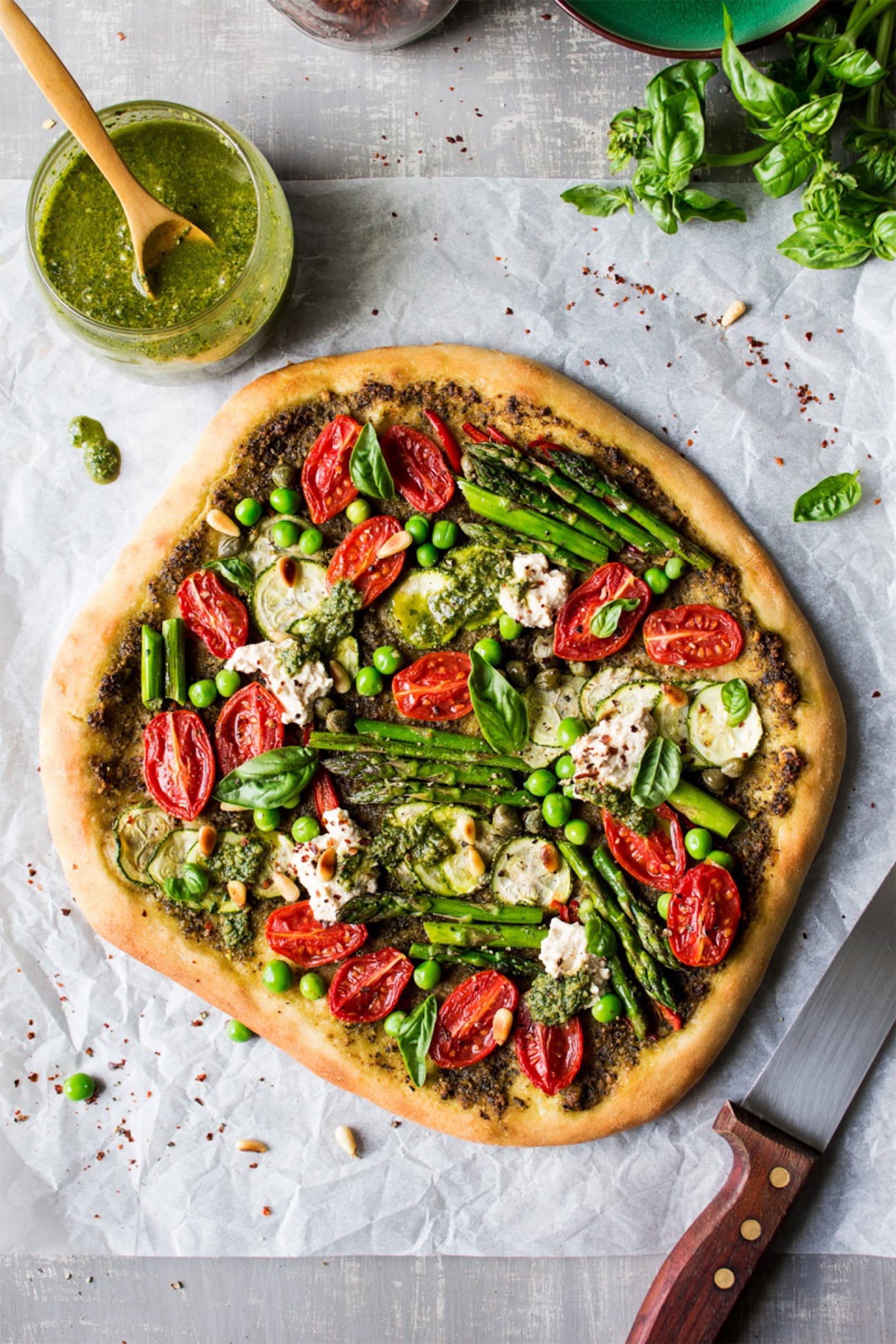 white board with cup of pesto and vegetable pizza with basil and asparagus