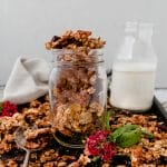 glass jar of banana bread granola on a tray next to a glass of milk