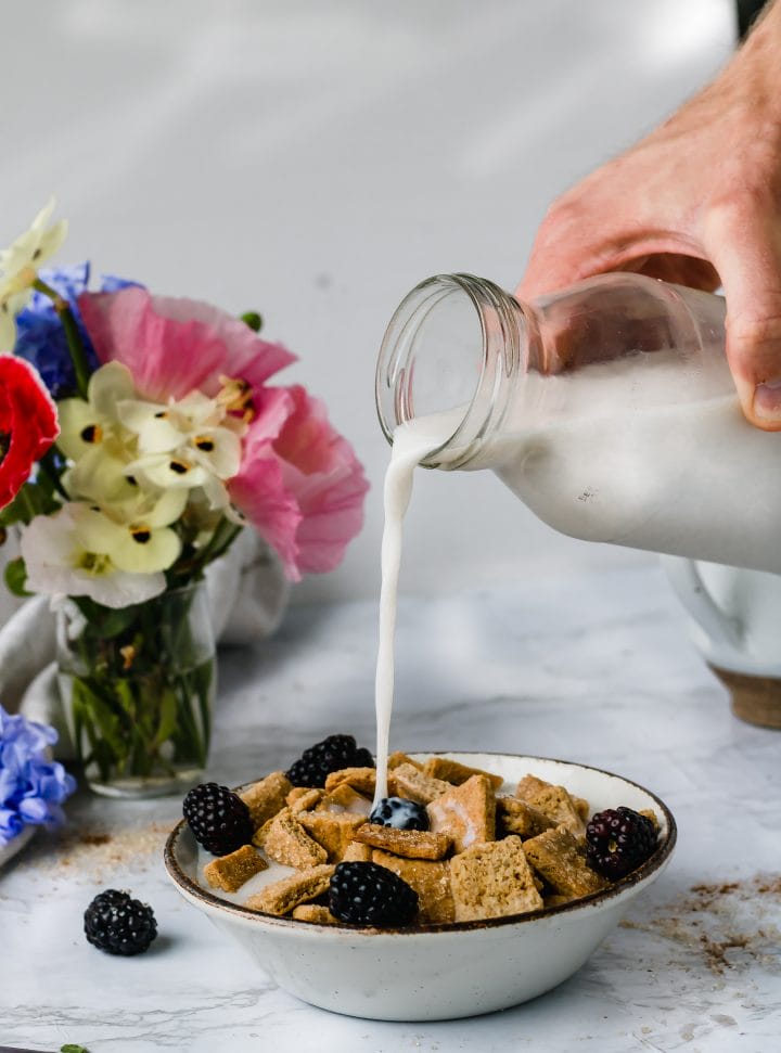 hand holding milk jug pouring into a bowl of homemade cereal with flowers in the background