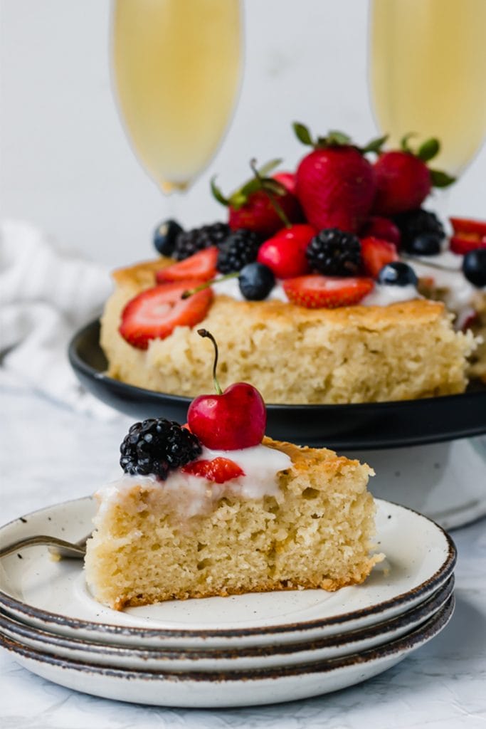 slice of white olive oil cake topped with berries with champagne in the background