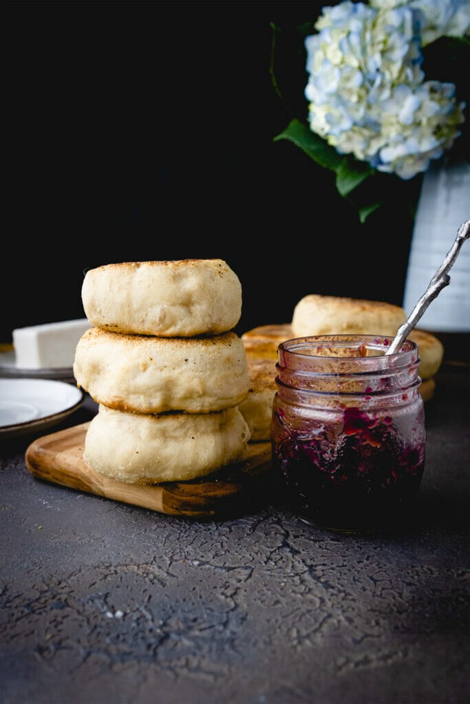 stack of three vegan english muffins next to a jar of jam on a tray