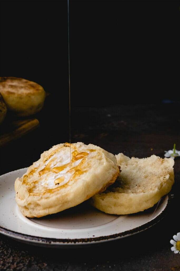 agave syrup being drizzled onto a cut open english muffin on a white place