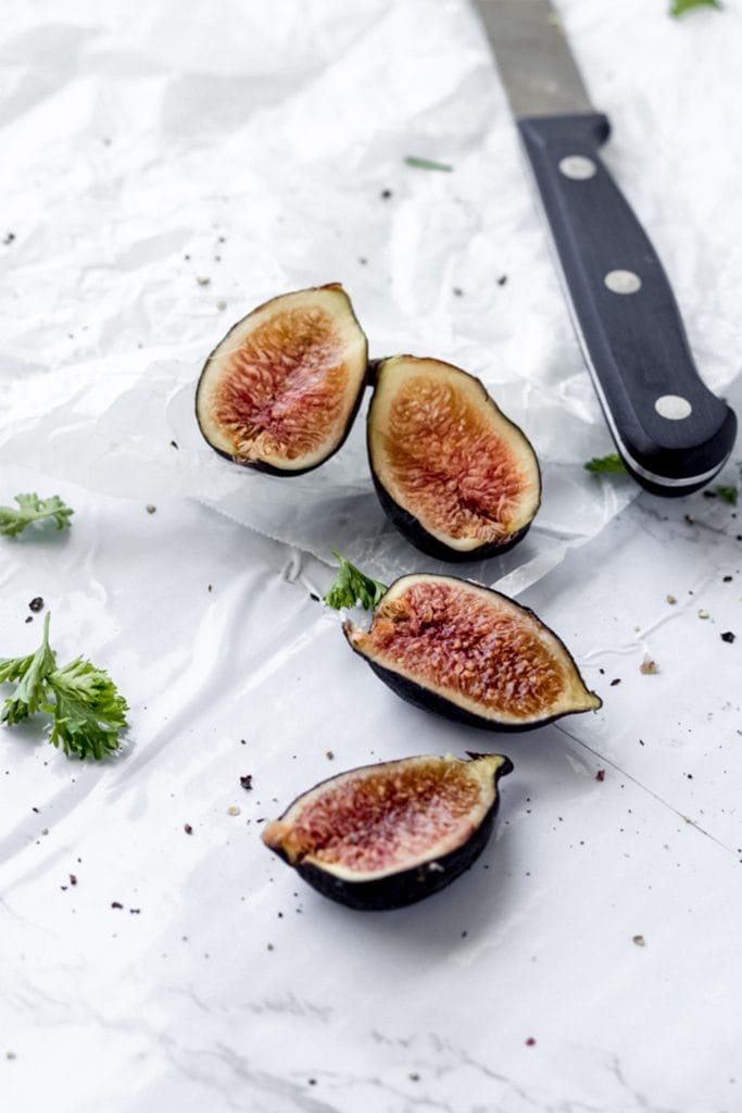 sliced figs on a white board with a knife in the foreground