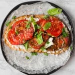 overhead shot of tomato toast with feat and basil on a black plate