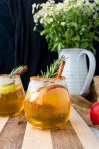 smoky apple cider sangria with cinamon, apple slices, and rosemary on a wood board