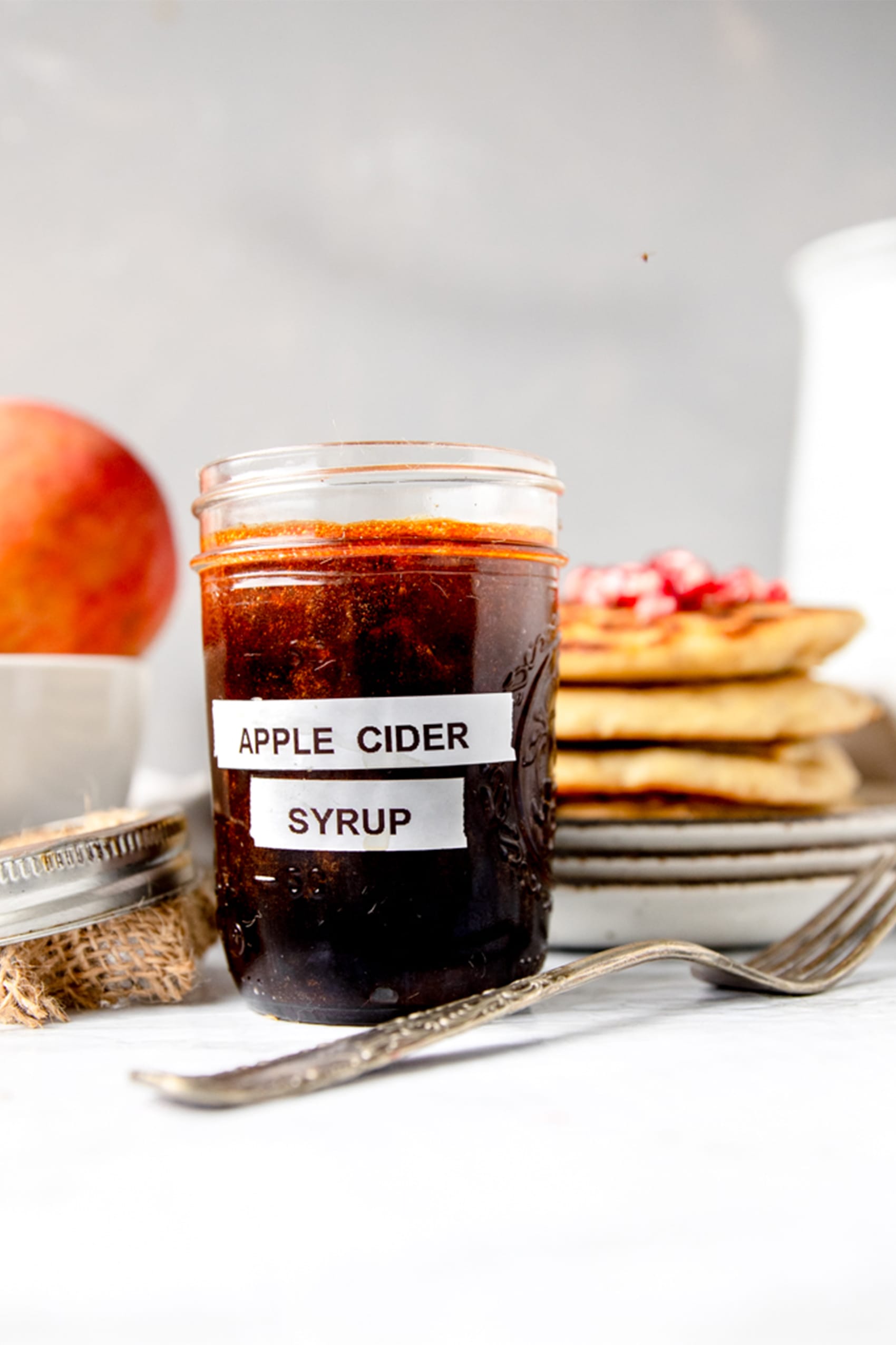 side view of glass ball jar labeled " apple cider syrup" next to an antique silver fork