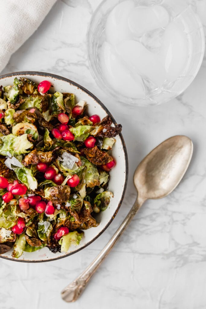crispy Brussels sprouts in a white bowl next to a glass of water