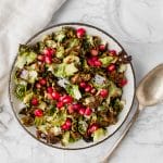 overhead shot of crisp Brussels with pomegranate on a marble board next to a silver spoon