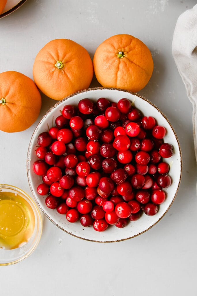 bowl of fresh cranberries in a white bowl next to some oranges