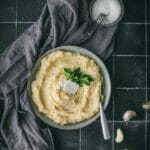 bowl of vegan mashed potatoes with a grey cloth on a black tile table