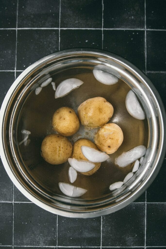 five golden potatoes in a stainless steel bowl ice bath