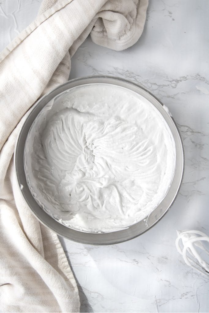 overhead shot of coconut whipped cream in a silver bowl next to a hand mixer