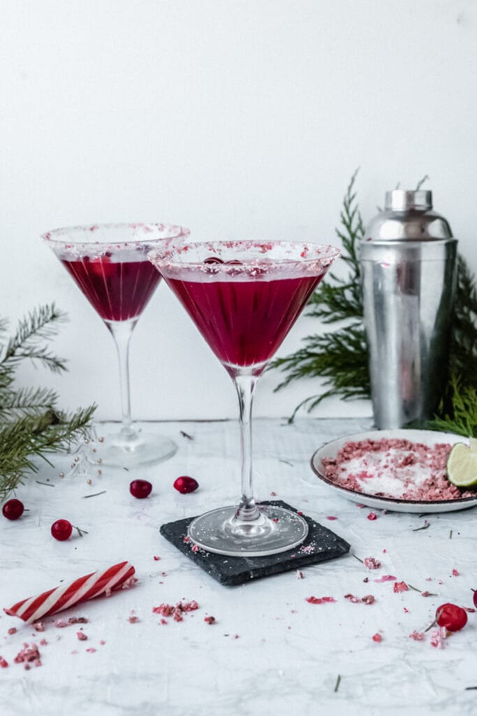two red cosmopolitans in martini glasses next to a candy cane and some pine branches