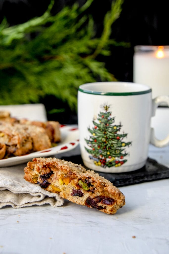 cranberry pistachio biscotti next to a christmas mug on a white table