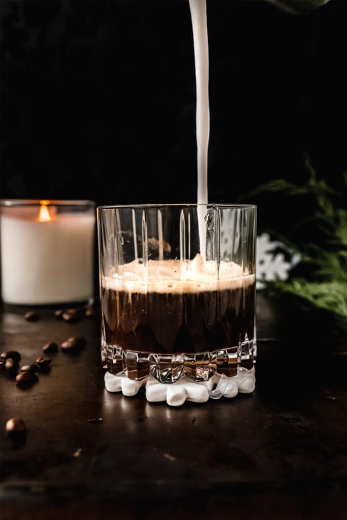 side view of a coffee cocktail with a stream of coconut cream going into it