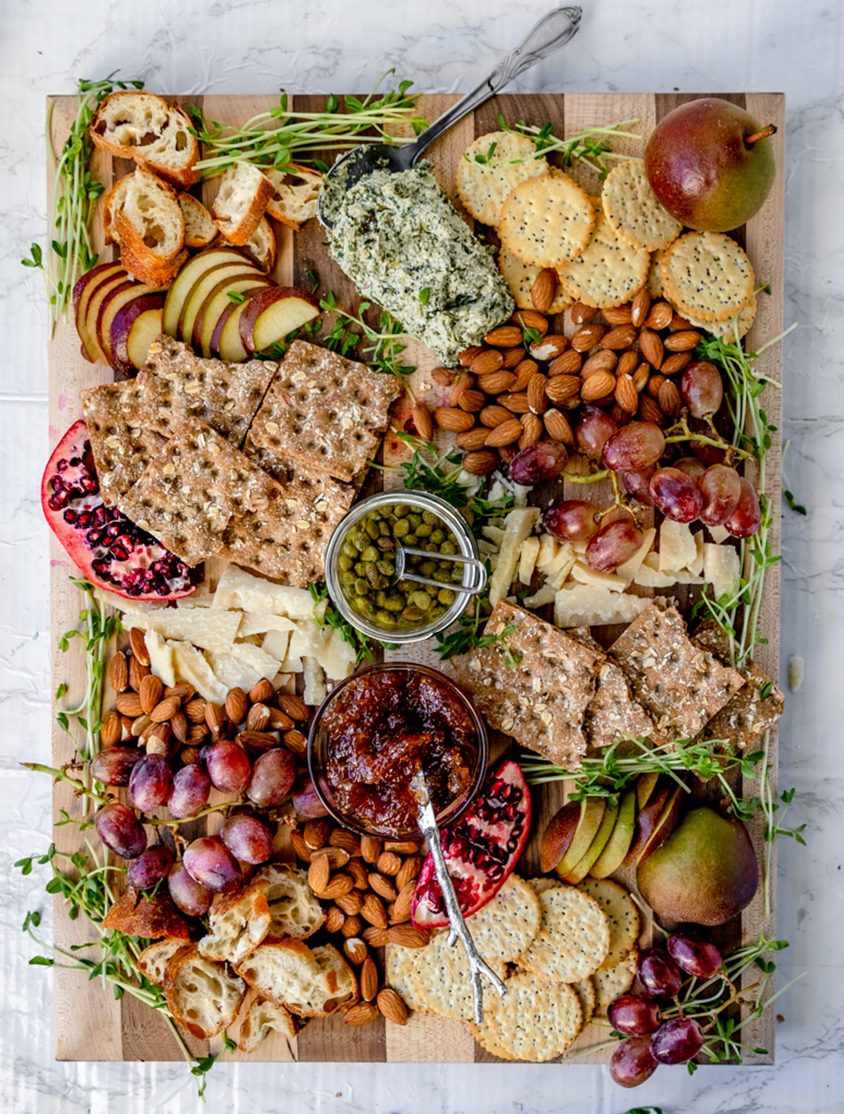 overhead shot of wooden cheese board with a variety of fruits, cheeses, and nuts in a purple green color scheme