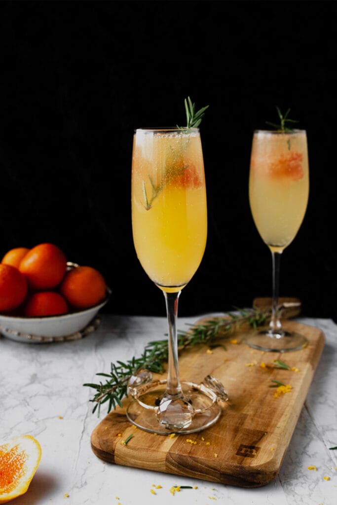 two flutes of orange mimosa cocktail on a wooden board