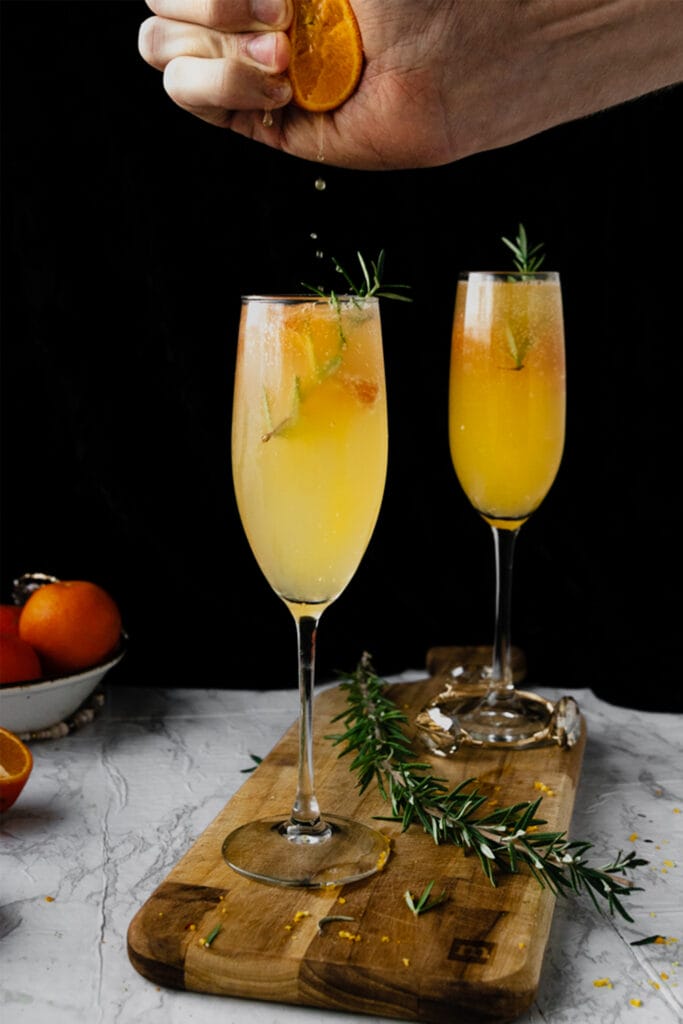 hand squeezing orange juice into champagne flute of mimosa