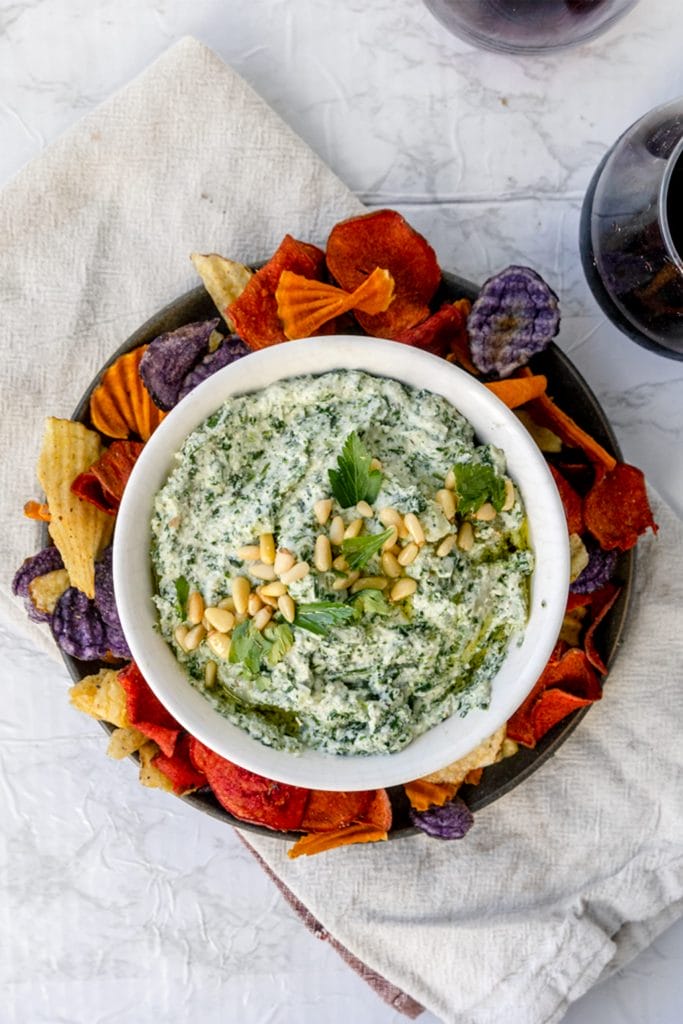Overhead shot of spanakopita dip in a white bowl surrounded by colorful chips