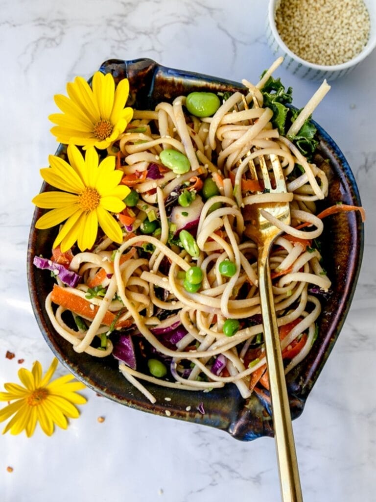 overhead shot of vegan sesame noodles in a blue bowl with a fork and sesame seeds