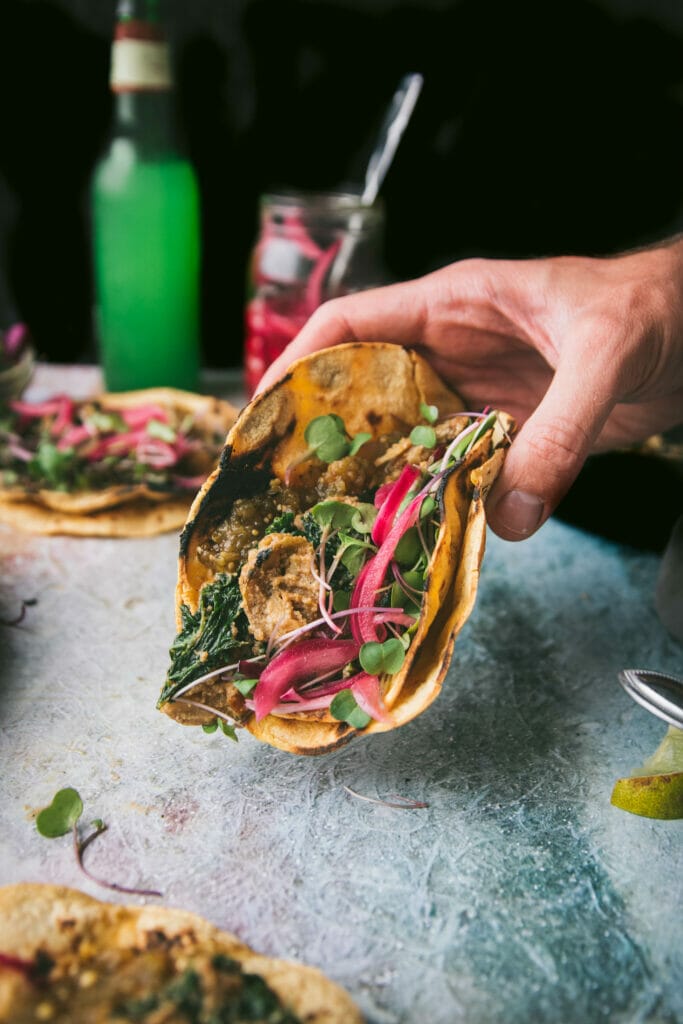 hand holding a creamy kale potato taco with pickled onions