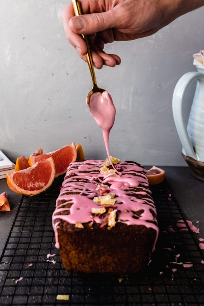 spoon drizzling icing onto vegan grapefruit poppyseed loaf cake