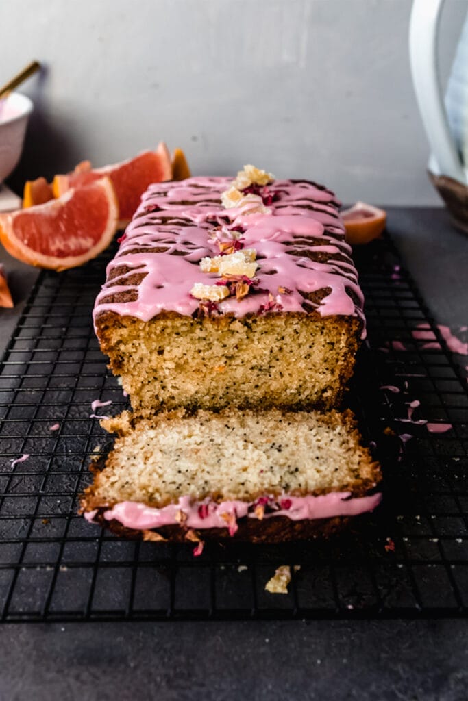 side view of grapefruit poppyseed loaf cake with pink icing and a slice cut out