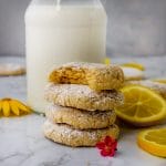 stack of bright vegan lemon crinkle cookies with a bite taken out next to a glass of milk