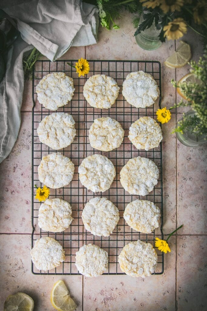overhead shot of vegan lemon crinkle cookies on a stone table next to yellow flowers and lemon wedges