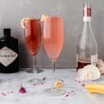 two rose french 75 cocktails on a marble table next to a bottle of wine and a bottle of gin