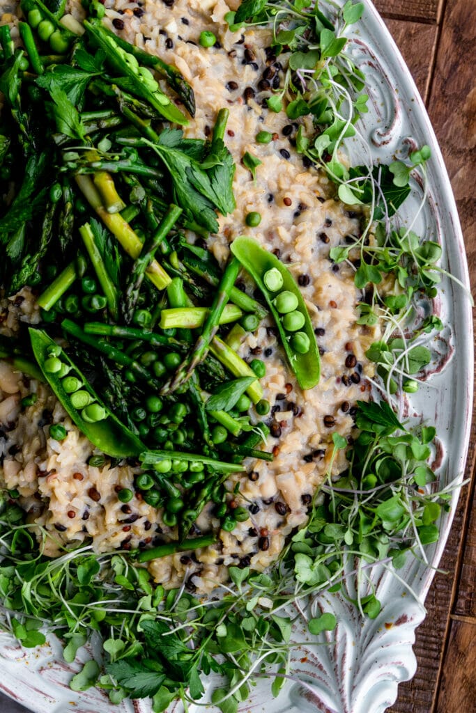 close up of barley risotto topped with asparagus and peas on a white plate