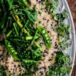 close up of barley risotto topped with asparagus and peas on a white plate