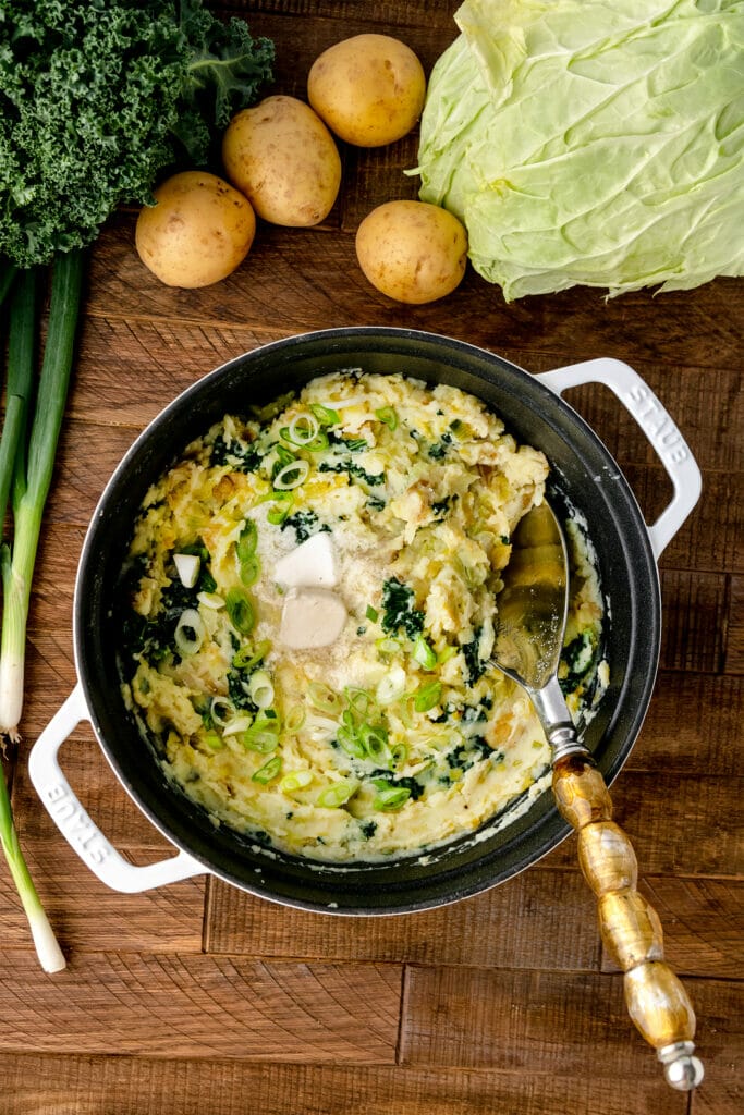 overhead shot of vegan colcannon with leeks in a white pot on a wooden table with a spoon 