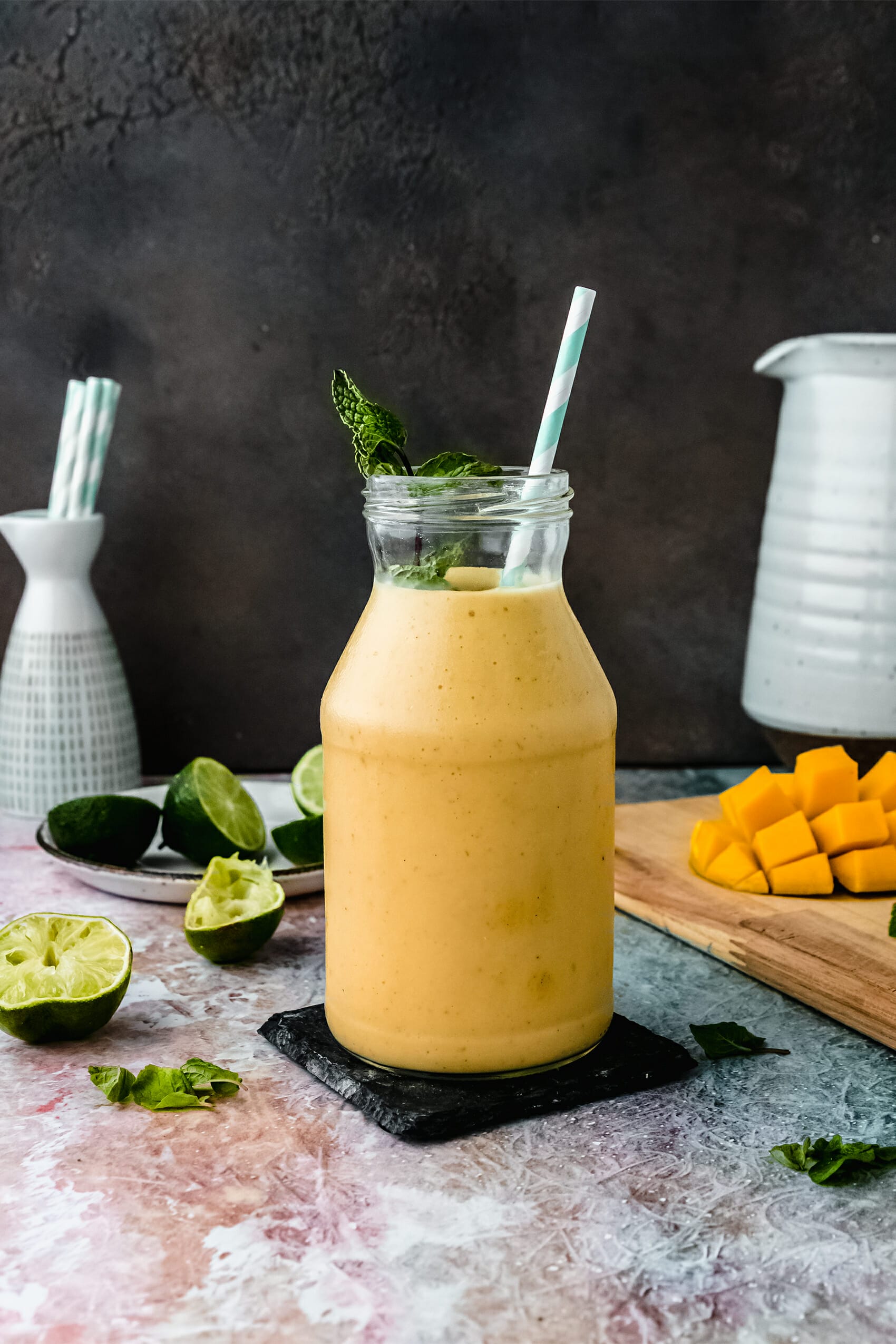 glass jar of vegan mango lassi on a table next to mango pieces