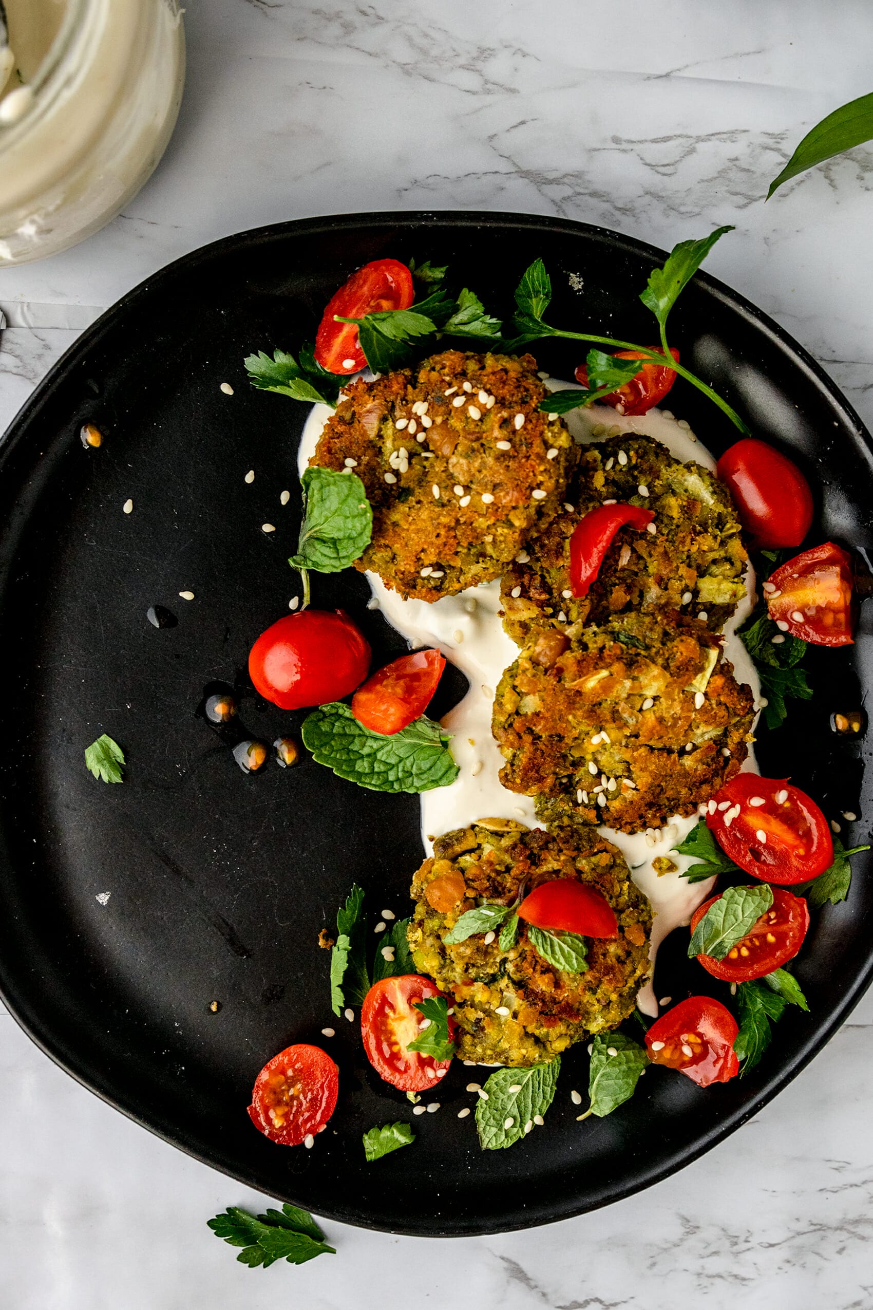 black plate with vegan pistachio baked falafel covered in cherry tomatoes and fresh herbs