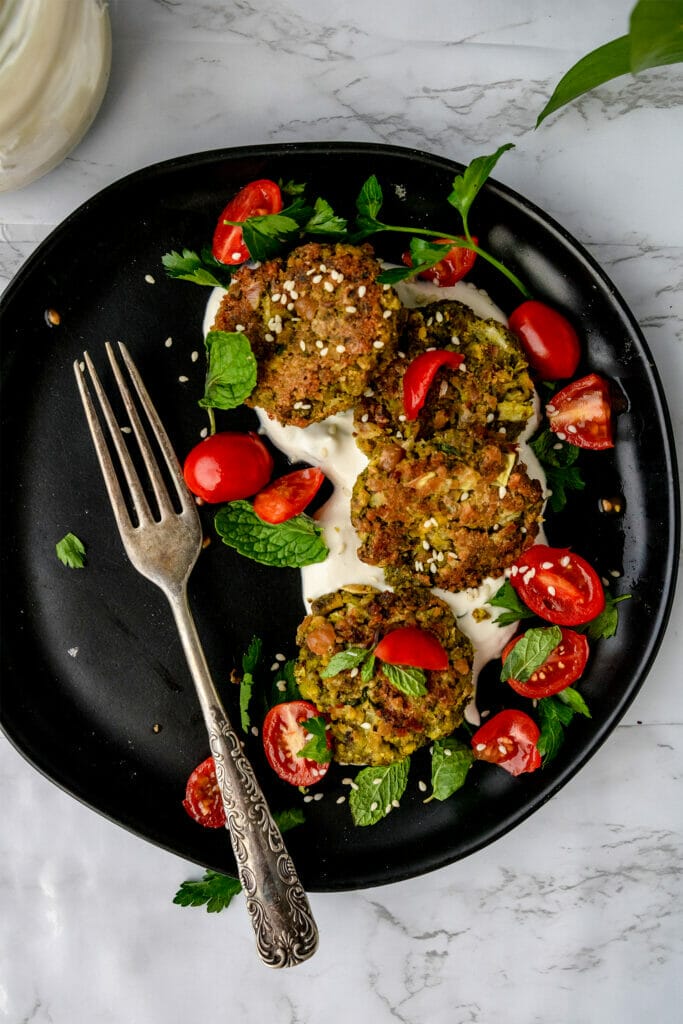 black plate with vegan pistachio baked falafel covered in cherry tomatoes and fresh herbs