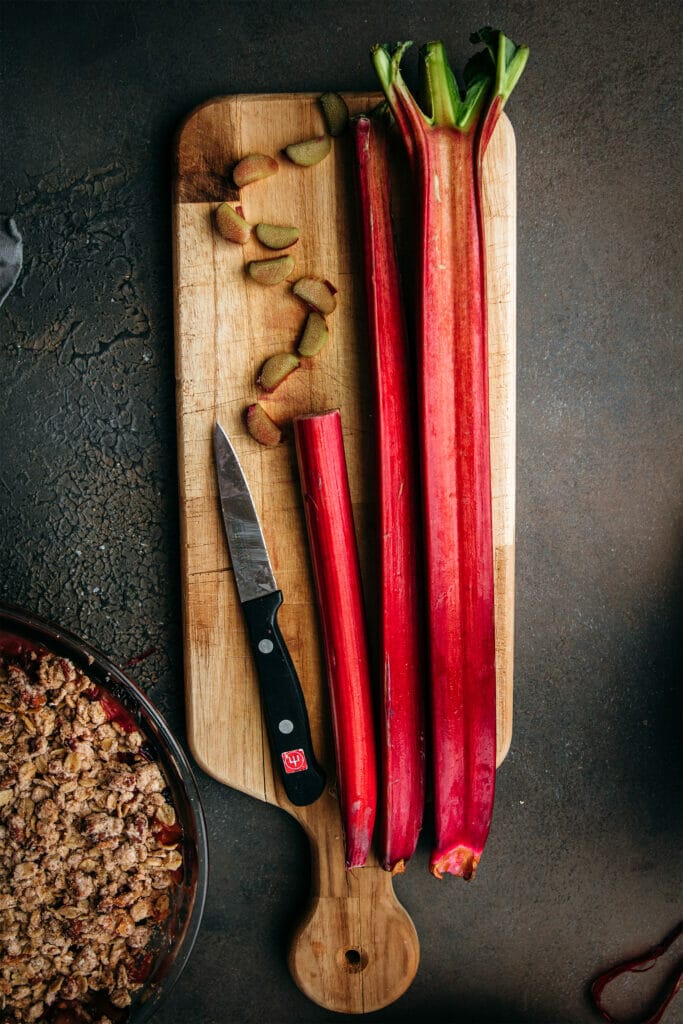 two stalks of red rhubarb with one sliced stalk on a wooden tray with a knife