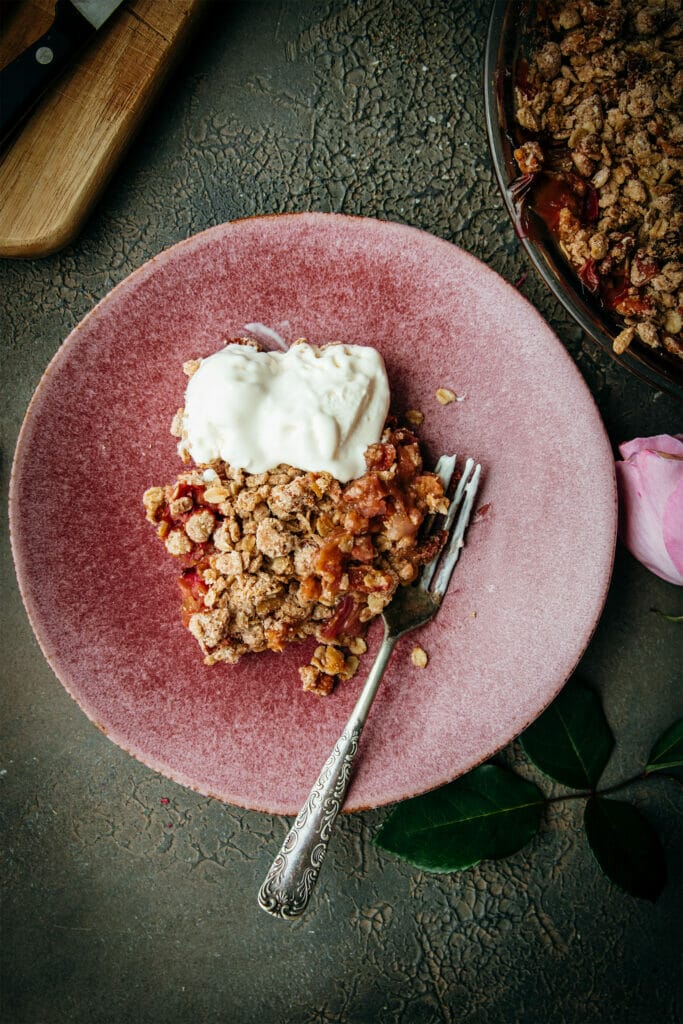 pink plate with a scoop of rhubarb crumble and ice cream