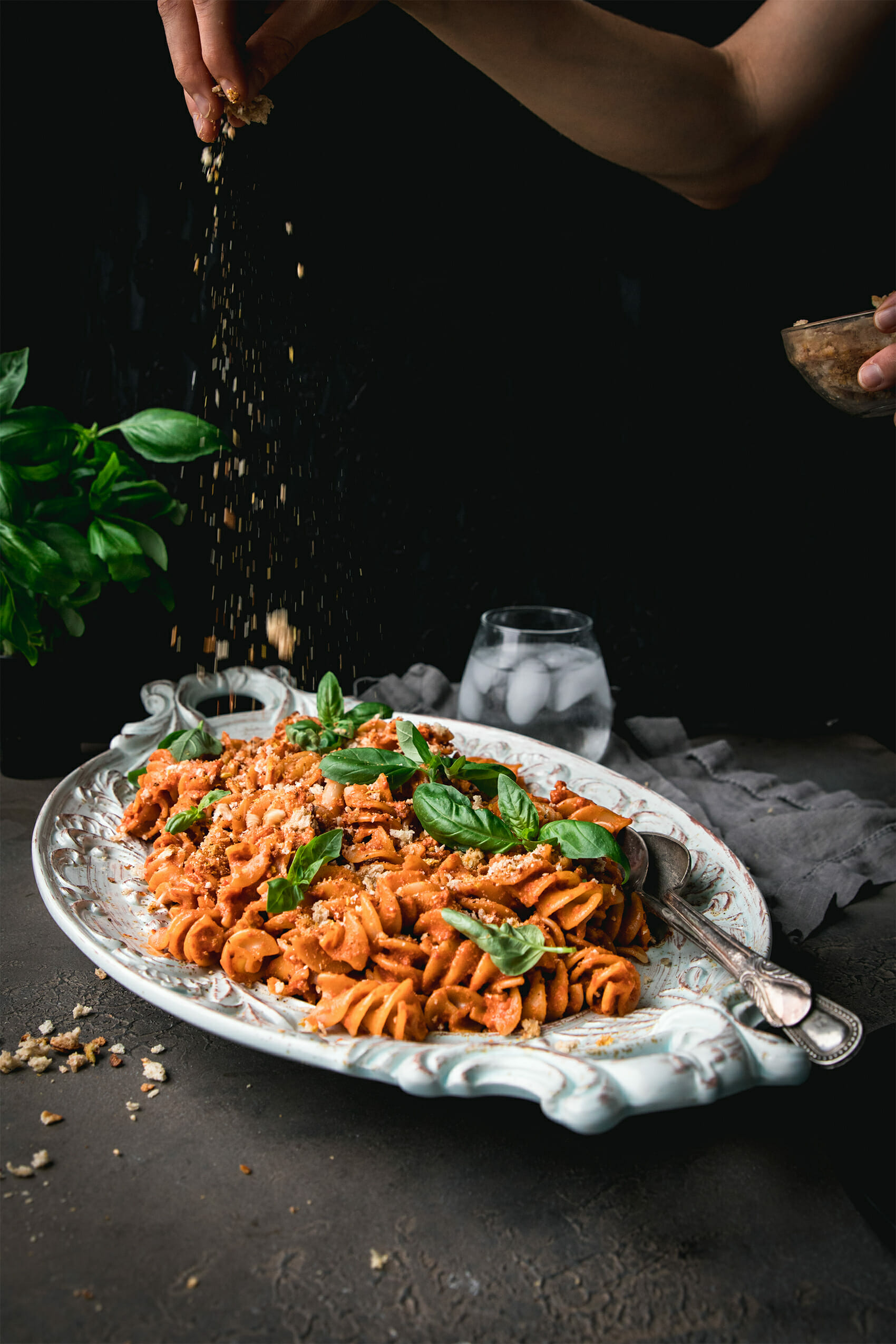 hand holding breadcrumbs sprinkled onto a plate of roasted red pepper pasta salad